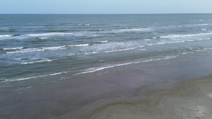 Serene Galveston, Texas beach with no visible people, clean sand, and evenly spaced wave lines approaching shore under clear horizon, emphasizing symmetry and untouched coastal beauty, vacation. USA