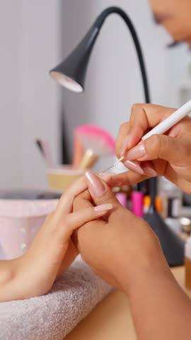 Close up of a manicurist applying gel nail polish and decorating a client's fingernails before using a uv lamp to cure the manicure