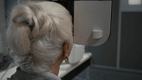 Back view shot of white haired senior woman looking into automated phoropter during eye exam in clinic with focus flowing from patient to eye chart projected on wall, copy space - Powered by Shutterstock - Get 15% off with code: PIKWIZARD15