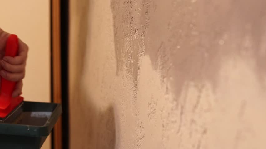 Painting a wall indoors, selective focus. Repainting a wall, hand with a wide brush close-up. Repair and painting work. Close-up of a woman's hand with a brush painting a wall with gray paint