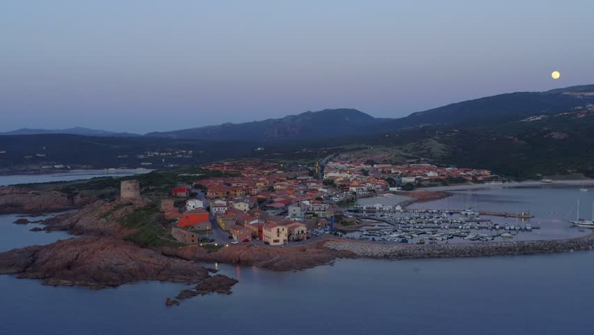 Aerial drone view of Castelsardo and Isola Rossa seaside town at sunset with a marina along the azure coastline of Sardinia, Italy