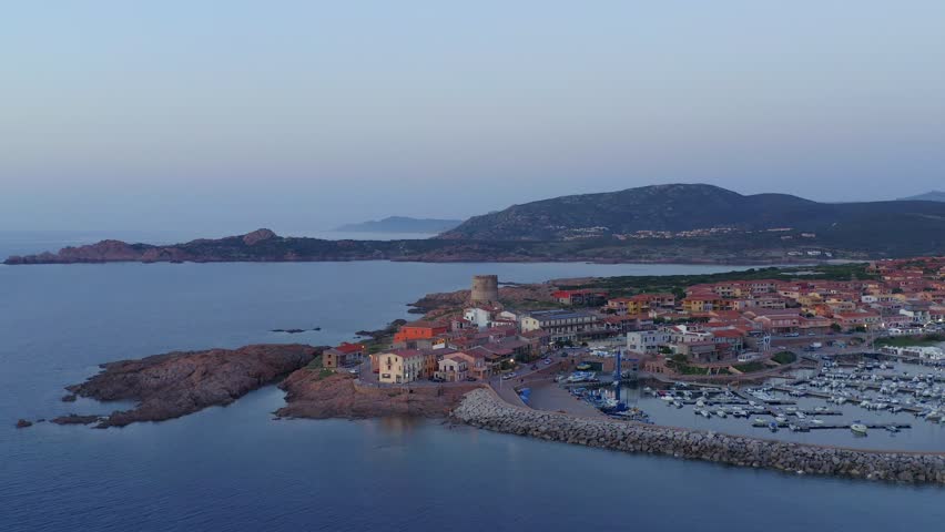 Aerial drone view of Castelsardo and Isola Rossa seaside town at sunset with a marina along the azure coastline of Sardinia, Italy