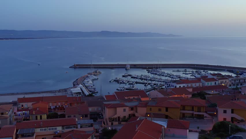 Aerial drone view of Castelsardo and Isola Rossa seaside town at sunset with a marina along the azure coastline of Sardinia, Italy