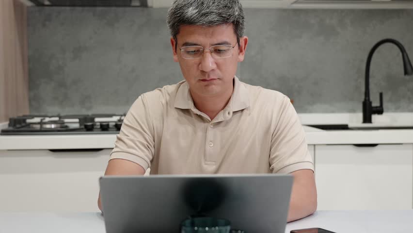 Adult man using voice command on his smartphone while working on laptop at home. Concept of digital communication, AI assistant, customer support, voice control, smart technology, modern remote work.