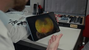Over shoulder close up shot of male doctor as ophthalmologist pointing at images on digital tablet screen during consultation in eye clinic, copy space - Powered by Shutterstock - Get 15% off with code: PIKWIZARD15