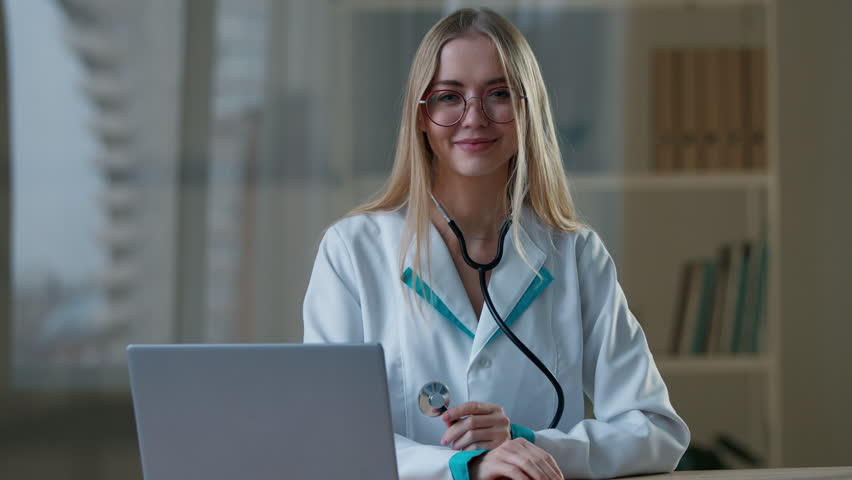 Caucasian woman female doctor posing in clinic showing stethoscope medical equipment in hospital at table with laptop computer girl nurse working looking at camera smiling pediatrician cardiologist