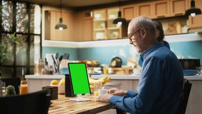 Vertical chroma key tablet with senior man enjoying morning routine, sitting at the table with toast and coffee. Checking device on the breakfast table, natural communication moment. Camera A. - Powered by Shutterstock - Get 15% off with code: PIKWIZARD15