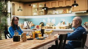 Mature man with physical disability serving coffee and pastry with wife, enjoying cozy morning routine with laughter and casual conversation. Positive household moment in modern home. Camera A. - Powered by Shutterstock - Get 15% off with code: PIKWIZARD15