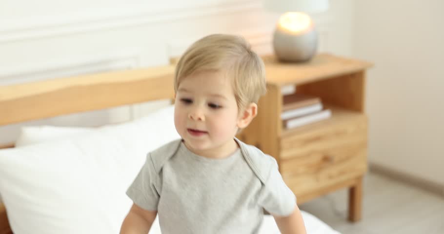 Cute little boy playing with toys on bed at home. Camera moving