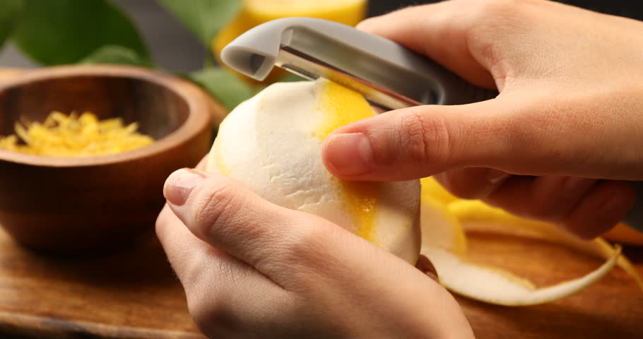 Woman peeling lemon zest at table, closeup