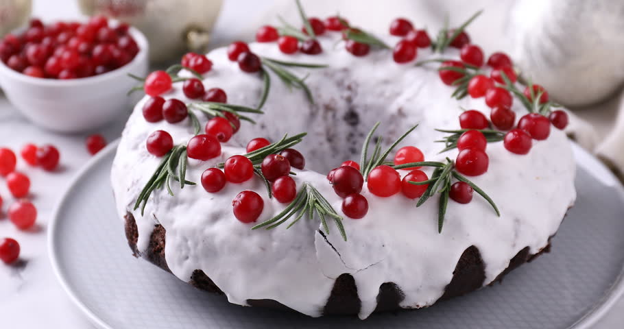 Woman cutting tasty Christmas cake with cranberries and rosemary at table, closeup