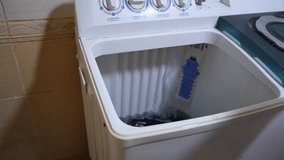 Close-up of a man's hand holding and dropping a purple shirt into an empty top-loading washing machine. Preparing for a domestic laundry wash cycle at home. - Powered by Shutterstock - Get 15% off with code: PIKWIZARD15