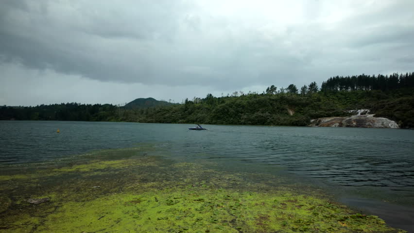 Small Boat On Calm Lake With Green Algae Shore