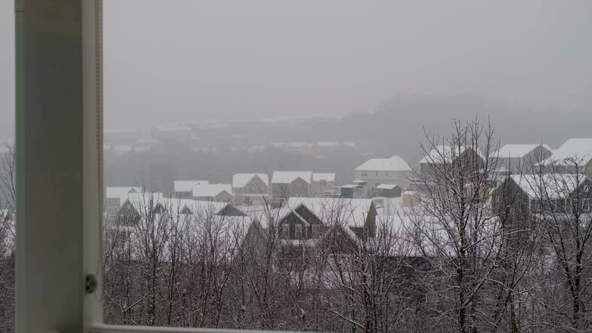 Snow covers homes and trees in a quiet neighborhood during a winter storm at midday