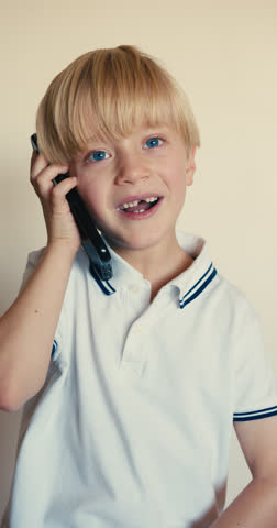 A blond boy with blue eyes talking on the phone, having an interesting and emotional conversation while smiling.