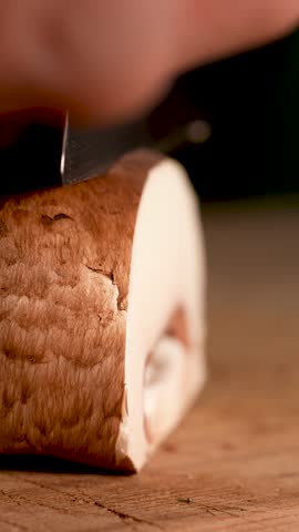 Slow-motion close-up of a champignon mushroom being sliced with a sharp knife. Gentle motion, fresh texture and clean separation emphasize the mushroom’s natural form and softness.