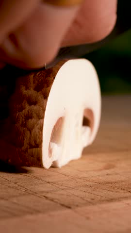 Slow-motion close-up of a champignon mushroom being sliced with a sharp knife. The gentle motion highlights fresh texture, clean separation and the natural form of the mushroom.