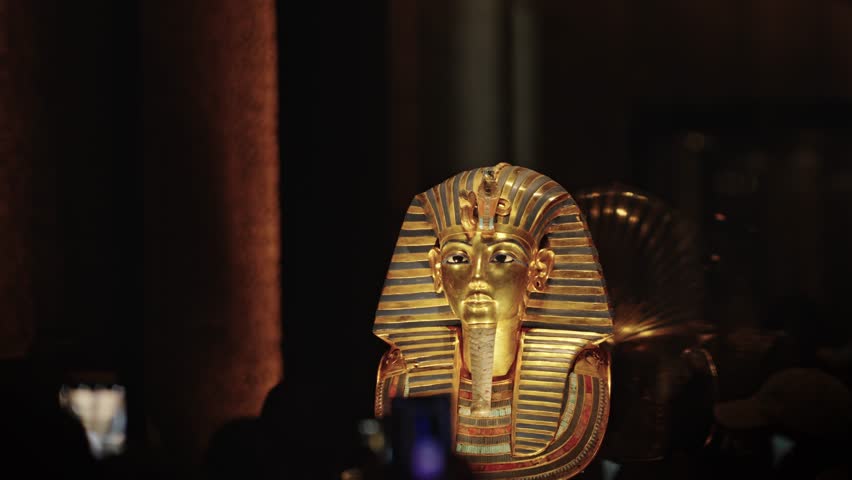 A dramatic close-up view of the legendary Gold Funerary Mask of Pharaoh Tutankhamun, displayed within the Grand Egyptian Museum (GEM).