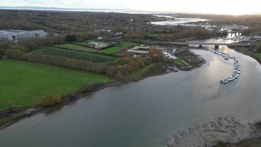 Aerial view capturing River Hamble curving through open countryside with green fields, autumn trees, moored boats, and calm water channels stretching across Hampshire landscape under soft daylight.