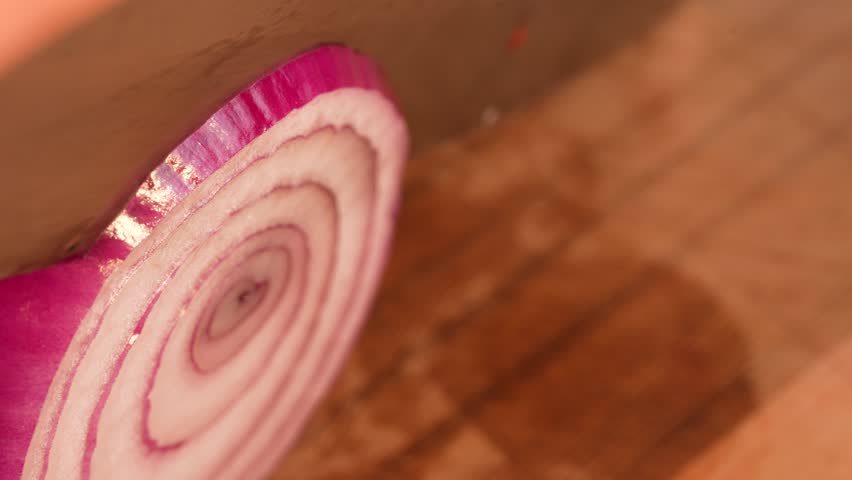Slow-motion close-up of a red onion as a thin slice is neatly cut off with a sharp knife. The layered structure and smooth knife movement emphasize the clarity, crispness and precision of the cut.
