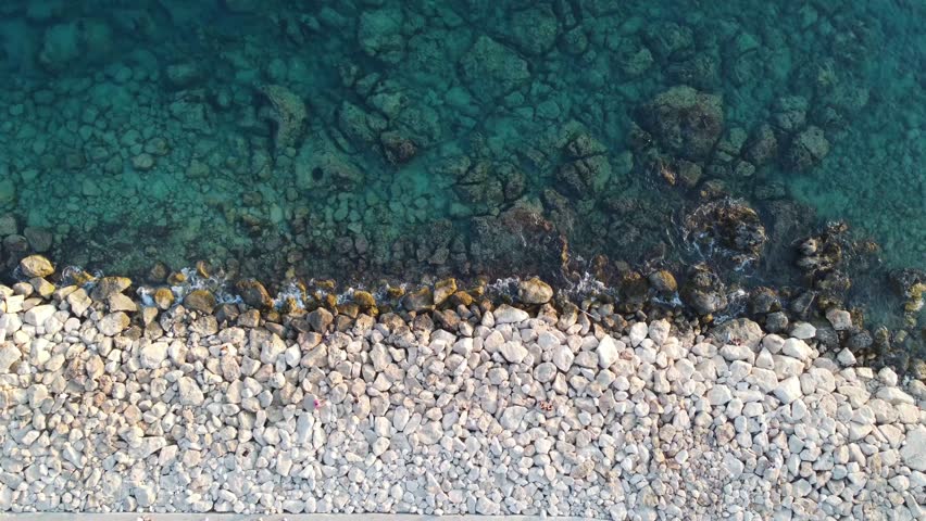 Aerial drone view showing rocky shoreline near Kas with clear blue green water and submerged stones, perfect for Social Media travel content and peaceful coastal nature scenes.