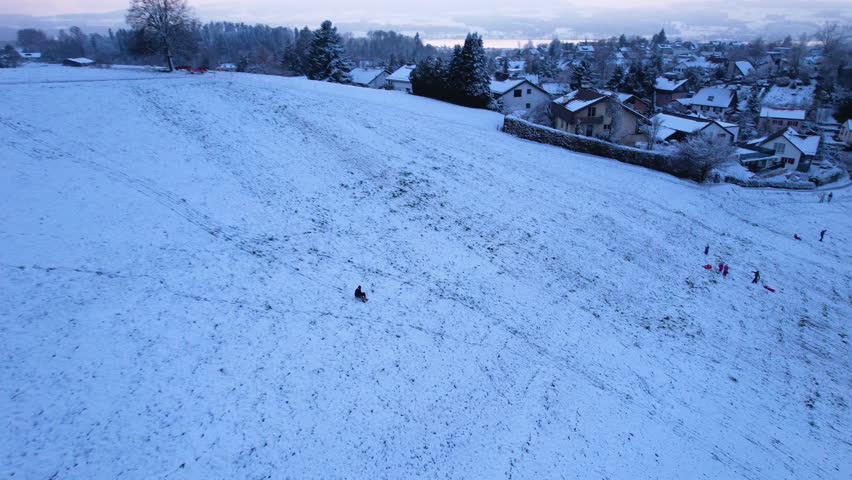 Following a man sledding down a snowy hill at sunset, Uster, Switzerland