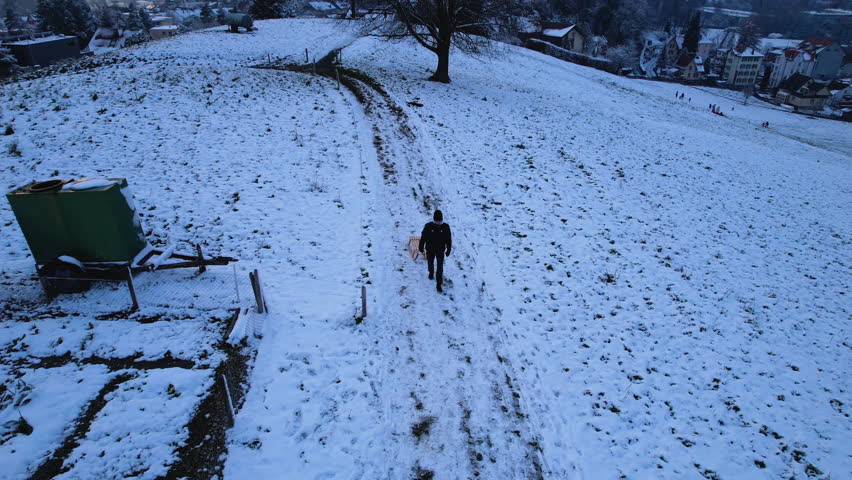 Young man with a wood sledge walking on top of a snowy hill, Uster, Switzerland