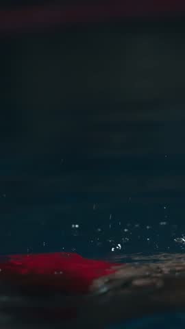 Focused female swimmer in red cap and goggles emerging from the pool, water droplets glistening on her face as she prepares for an intense training session