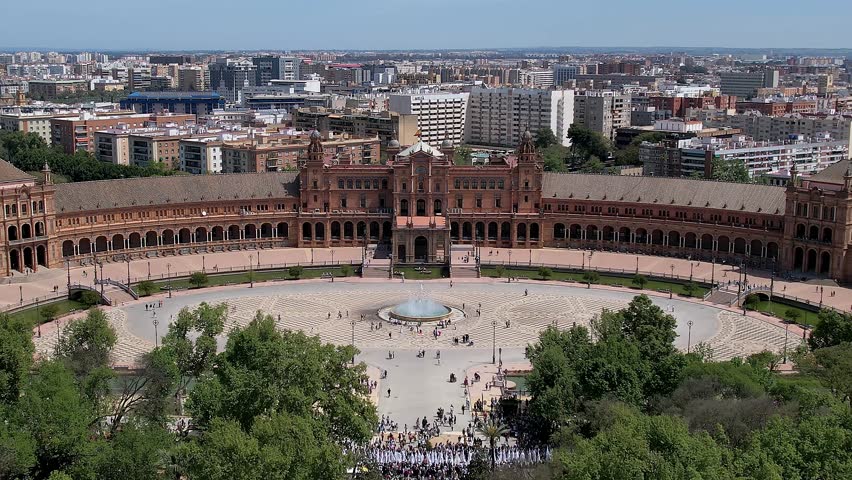 Drone zooming out in Plaza de Espana in Parque de María Luisa in Seville, Spain, Historical landmark and architectural masterpiece, Showcasing iconic buildings and greenery with city skyline expanding