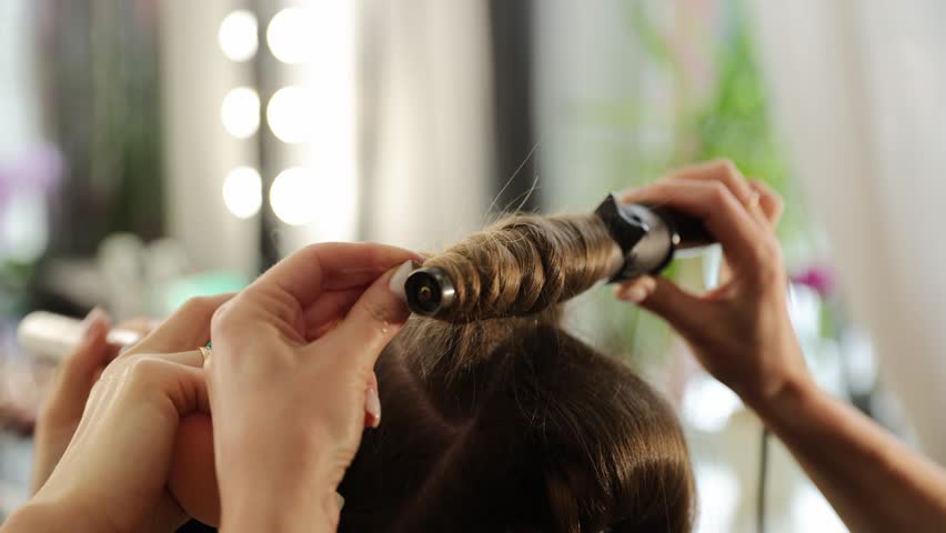 Hairdresser styling woman's hair with a curling iron