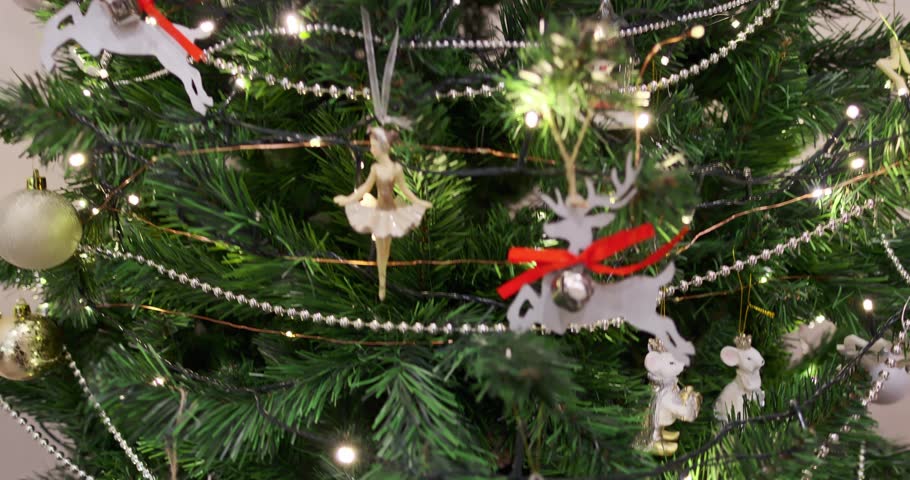 Woman hand decorating green Christmas tree with silver baubles, gold beads chain, festive holiday tree and toys. Christmas tree decorations. Decorating Christmas tree. New Year spirit.