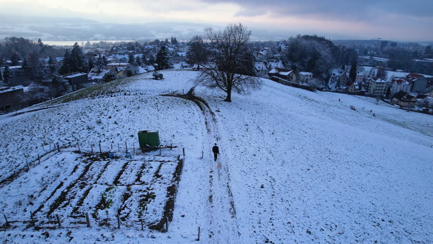 Aerial of a man walking on a snowy hill with a wood sledge, Uster, Switzerland