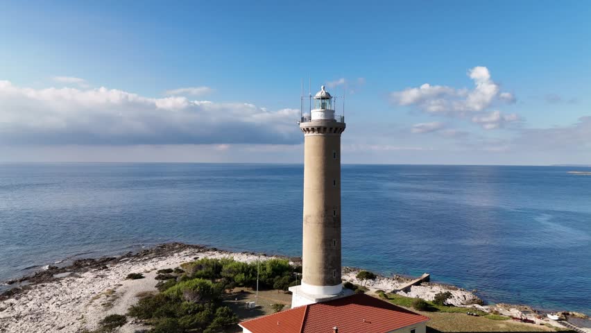 Rotating drone aerial around lighthouse tower of the Veli Rat on Dugi Otok, Croatia.Coastline with turquoise Adriatic Sea, and bright sunny weather in Zadar county.