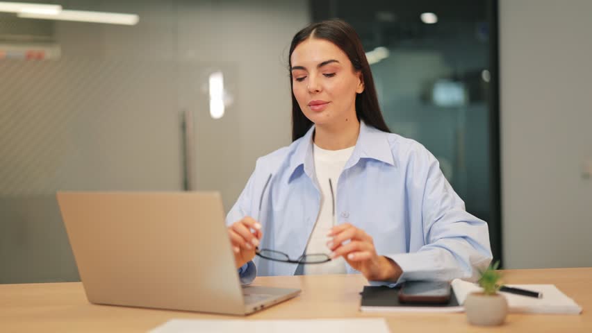 Professional woman in modern office, concentrated on laptop. Exhibiting dedication and pleasant demeanor, efficiently completes tasks, creating successful outcomes. Focused work brings satisfaction.
