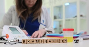 Wooden blocks spell word Examination near monitor with urine sample and stethoscope on desk. Woman clinician writes report recording patient data - Powered by Shutterstock - Get 15% off with code: PIKWIZARD15