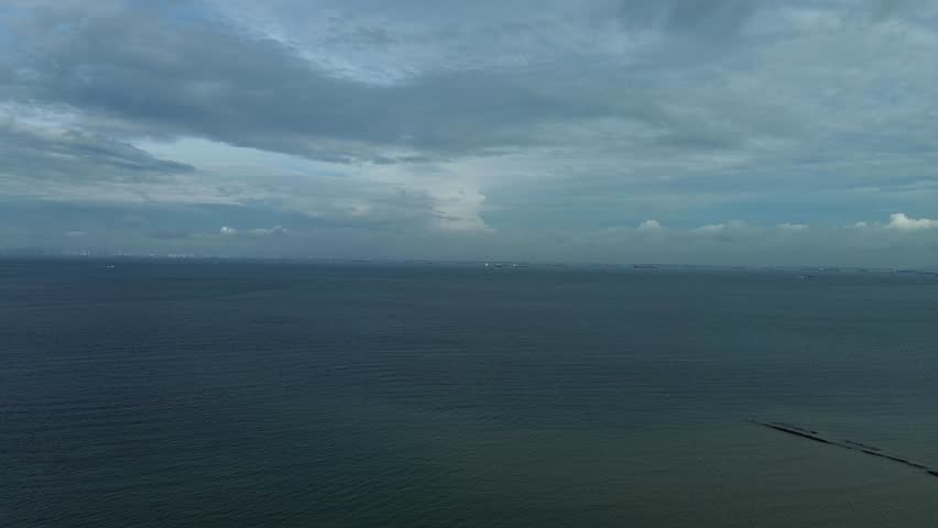 Vast expanse of sea under a cloud-covered sky, with distant maritime activities in the vast expanse of sea