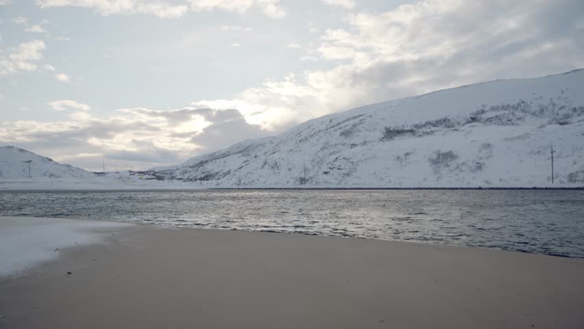 snow-covered hills sea bay with sandy beach. sunset clouds behind mountains