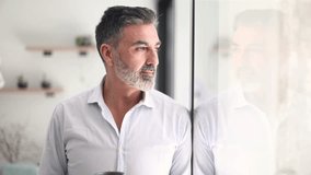 Pensive middle aged man with a gray beard looking out the window. Thoughtful successful entrepreneur enjoying a moment of reflection and a coffee break - Powered by Shutterstock - Get 15% off with code: PIKWIZARD15