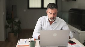 Middle aged professional man using a laptop and analyzing business documents. Freelancer working in his home office at a modern desk - Powered by Shutterstock - Get 15% off with code: PIKWIZARD15