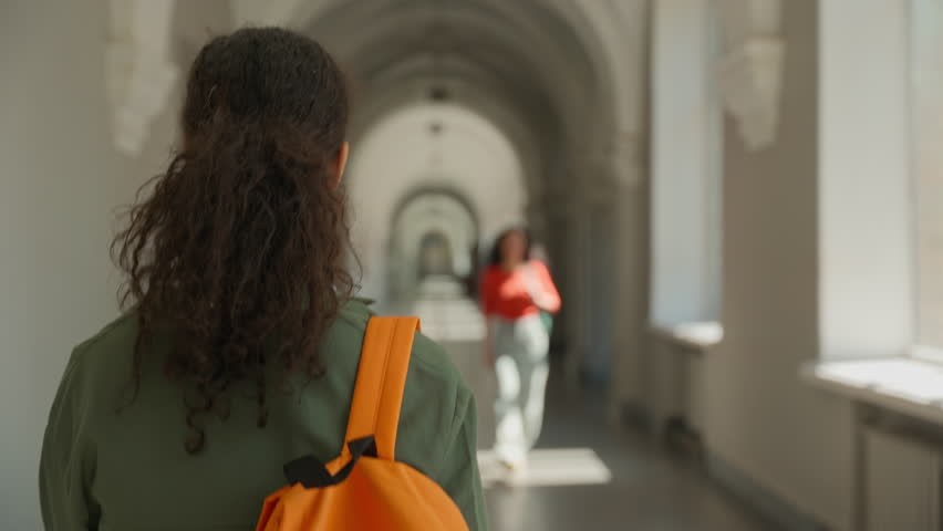 Two Hispanic females students meeting university corridor give high five smiling girls women multiracial friends campus college academy walking going greeting hello back view girl walk meet classmate