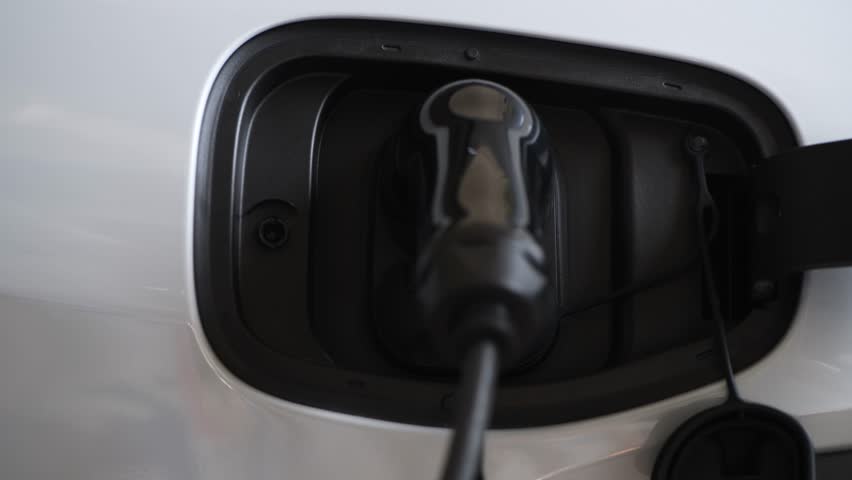 A man is disconnecting the charger cable to charge the electric car battery.