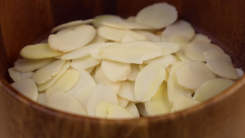 White almond petals falling down into the wooden bowl close up