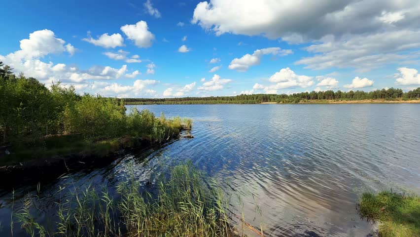 A Tranquil Lakeside Scene Under a Vast Blue Sky with Fluffy Clouds and Lush Green Surroundings Highlighting Nature
