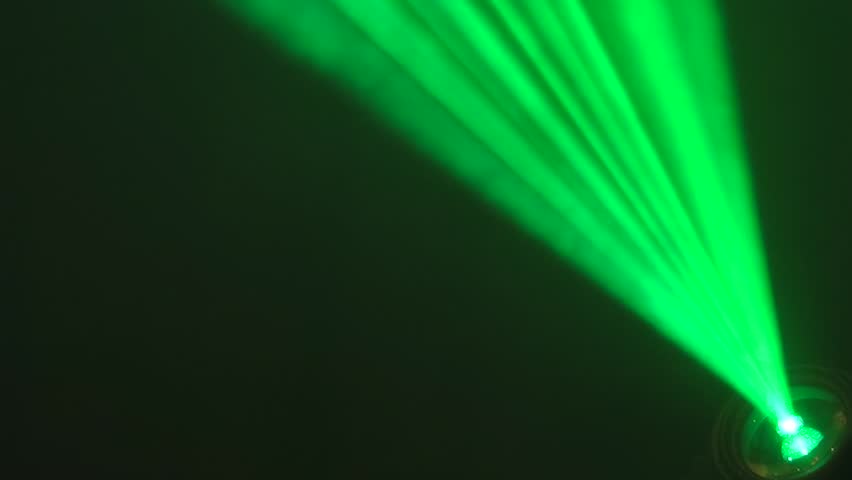 Vivid green and yellow laser beams project from a stage spotlight in a dark environment, creating a dramatic lighting effect with ample copy space.