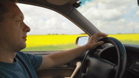 Middle-aged man putting on his sunglasses while driving a car on a country road with a beautiful yellow rapeseed field and a cloudy sky visible through the window on a sunny day - Powered by Shutterstock - Get 15% off with code: PIKWIZARD15