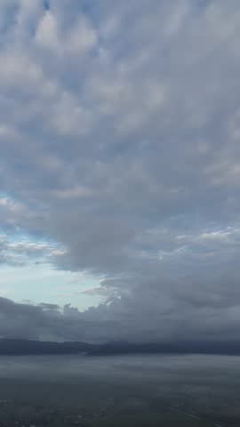 Dark storm clouds meet misty mountain valley. Atmospheric aerial scene with thick fog and dramatic weather.