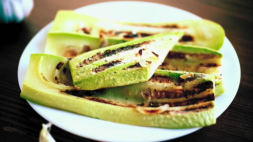 Grilled zucchini served with onions on a plate, presented on a table as a simple, flavorful, and healthy vegetable dish.