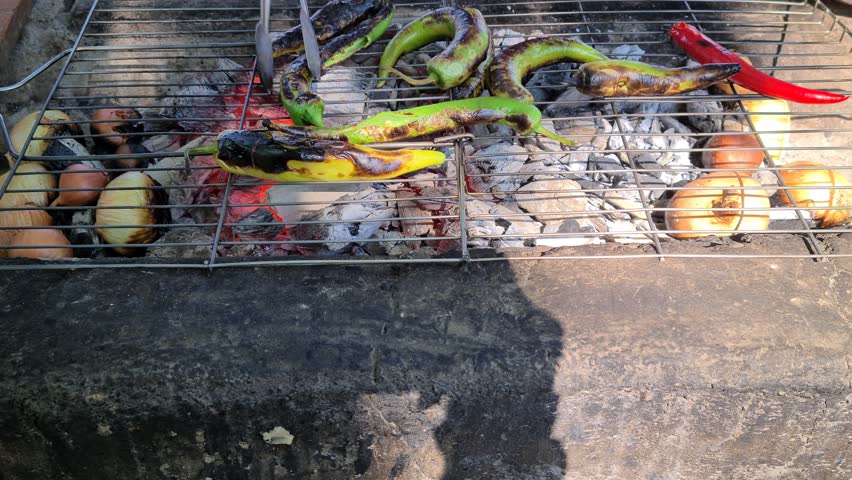 Red peppers, green peppers, and dried onions are cooking on the grill.