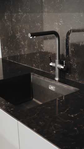Vertical video. Black kitchen sink and faucet. Modern kitchen interior with black marble. Black ceramic tiles on the wall and countertop.