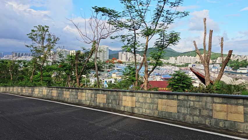 Scenic panoramic view of Sanya from Deer Turned Head Park, featuring a modern skyline, marina, mountains, lush greenery, and waterfront under a bright tropical sky.